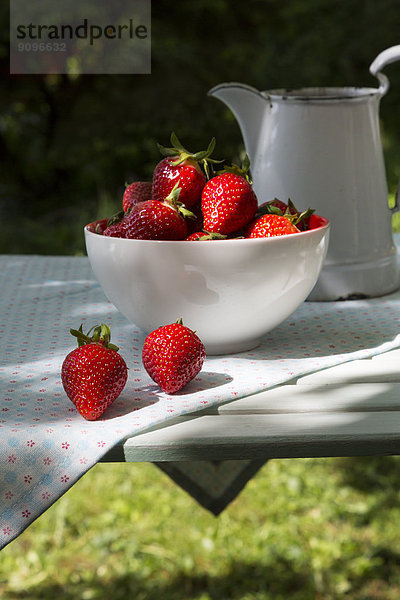 Schale mit Erdbeeren und Glas auf Tuch im Garten