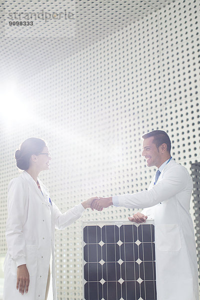 Wissenschaftler beim Händeschütteln am Solarpanel im Labor