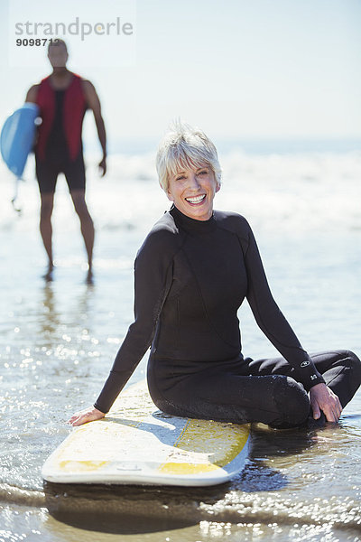Porträt der Seniorin auf dem Surfbrett am Strand