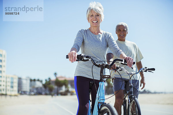 Porträt eines Seniorenpaares mit Fahrrädern an der Strandpromenade