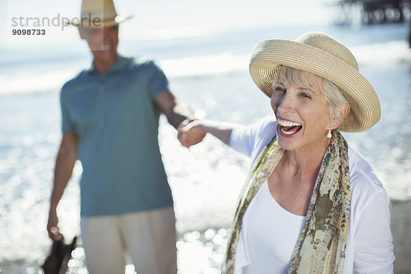 Enthusiastisches Seniorenpaar hält Hände am sonnigen Strand