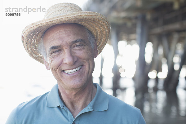Porträt eines lächelnden älteren Mannes mit Sonnenhut am Strand