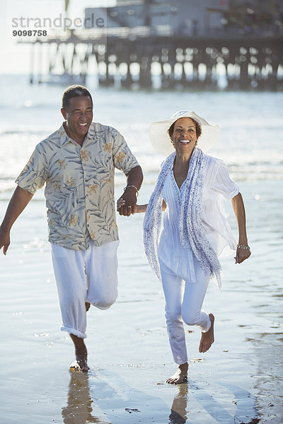Lächelndes Seniorenpaar rennt am sonnigen Strand