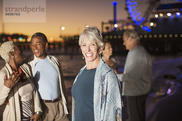Porträt einer begeisterten Seniorin mit Freunden am Strand bei Nacht