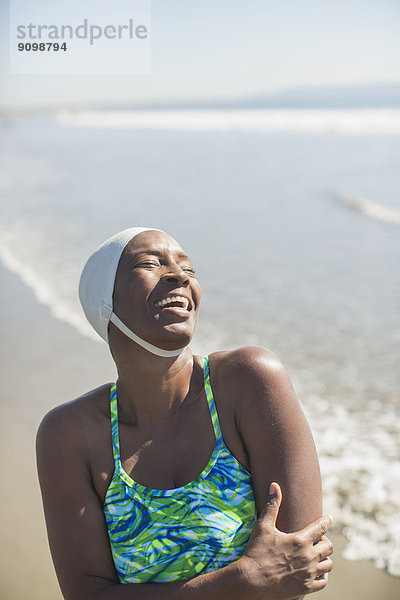 Frau im Badeanzug und Mütze lachend am Strand