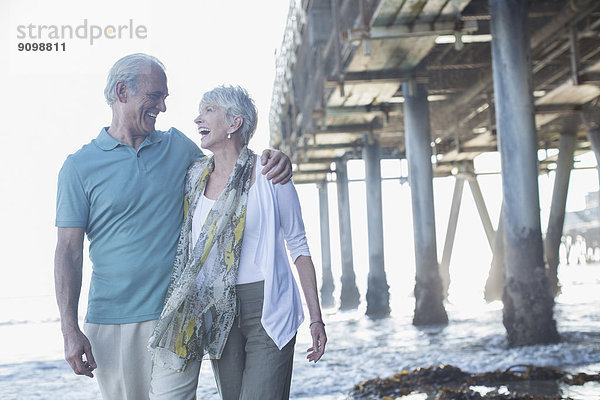 Seniorenpaar lacht beim Pier am Strand