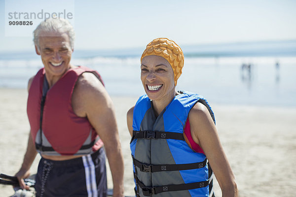 Enthusiastisches Paar in Schwimmwesten am Strand