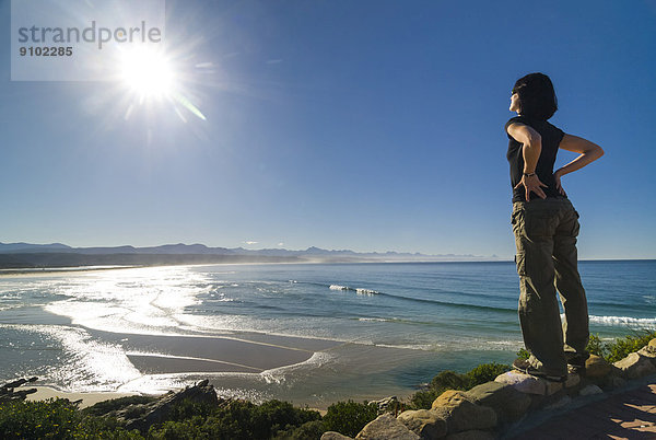 Junge Frau blickt auf eine Bucht und den Indischen Ozean  Plettenberg Bay oder Plettenbergbaai  Garden Route  Distrikt Eden  Provinz Westkap  Südafrika