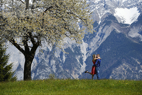 Liebespaar umarmt sich neben einem blühenden Baum im Frühling  hinten Berge  Tirol  Österreich