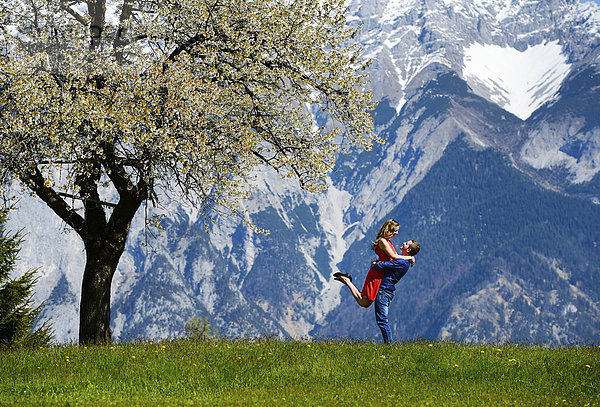Liebespaar umarmt sich neben einem blühenden Baum im Frühling  hinten Berge  Tirol  Österreich