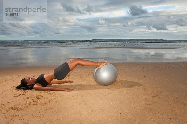 Junge Frau beim Yoga mit Übungsball am Strand