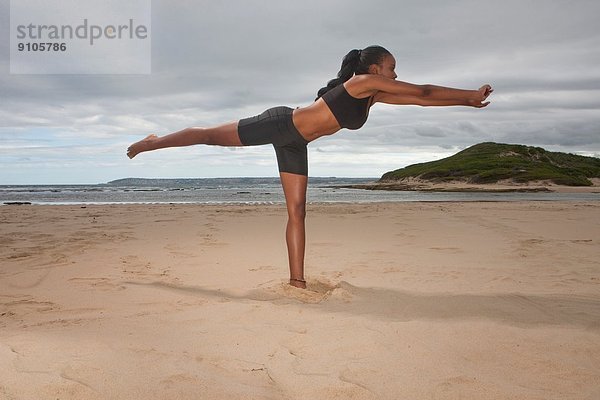 Junge Frau beim Yoga auf einem Bein am Strand