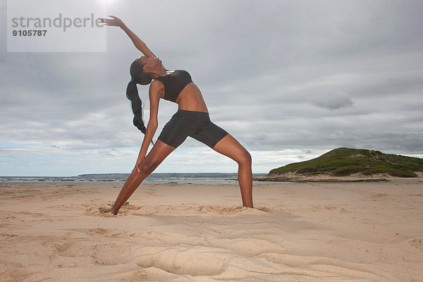Junge Frau praktiziert Yoga-Position am Strand