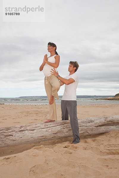 Schwangere mittlere erwachsene Frau mit Personal Trainerin  die Yoga am Strand praktiziert.