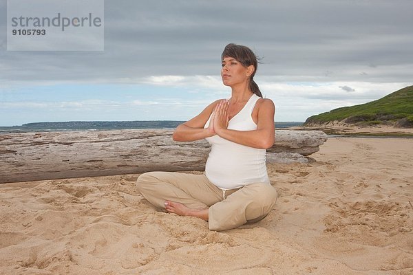Schwangere mittlere erwachsene Frau  die Yoga am Strand praktiziert.