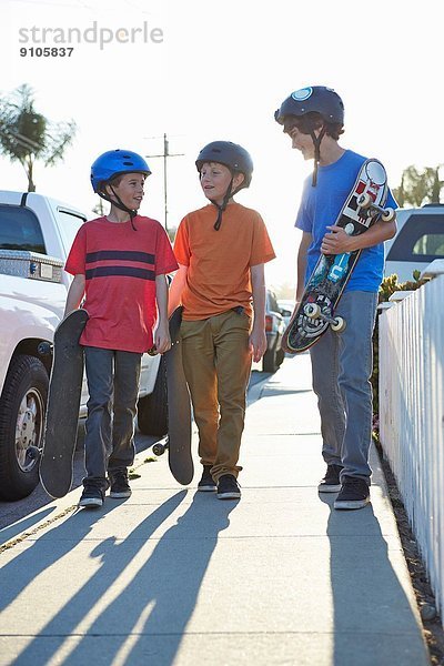 Jungen  die mit Skateboards den Bürgersteig hinuntergehen.