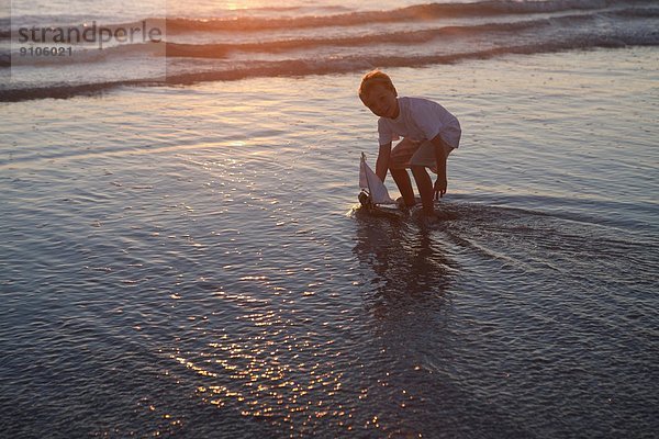 Junge spielt Spielzeugboot am Strand