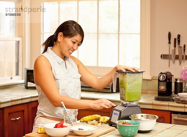 Junge Frau macht grünen Smoothie in der Küche