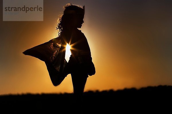 Silhouette des jungen Mädchens in geflügeltem Feenkostüm bei Sonnenuntergang