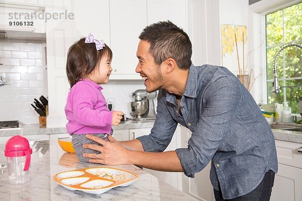 Mittelgroßer Mann mit Kleinkind-Tochter auf Küchenarbeitsplatte