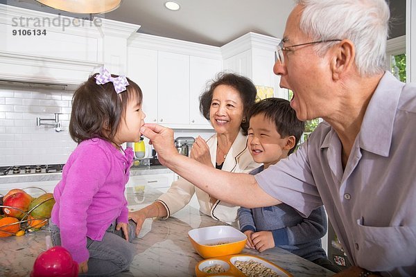 Großvater füttert Kleinkind-Enkelin in der Küche mit Snacks