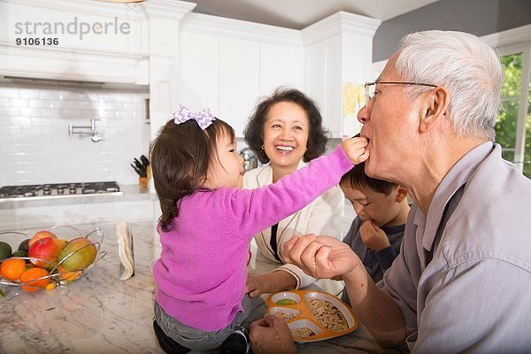 Weibliches Kleinkind füttert den Großvater in der Küche