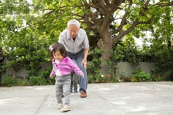 Großvater spielt Hopscotch mit Kleinkind-Enkelin