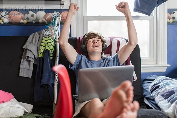 Teenager-Junge sitzt auf Stuhl mit Laptop-Computer  Arme angehoben
