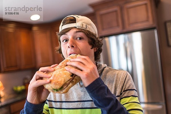 Teenager-Junge in der Küche beißt großes Sandwich