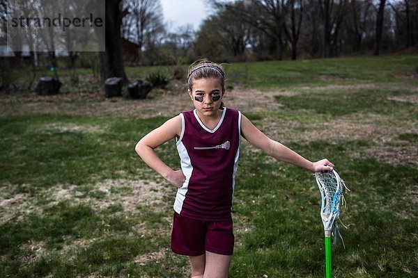Mädchen in Lacrosse-Uniform  an Lacrosse-Stick gelehnt