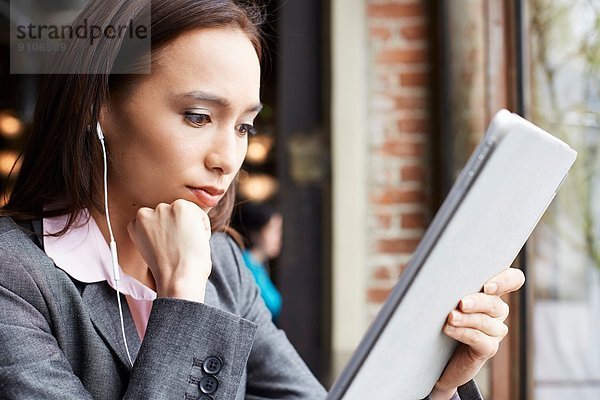 Junge Geschäftsfrau mit Kopfhörern beim Lesen von Papierkram im Café