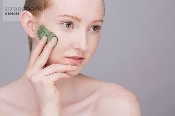 Porträt einer jungen Frau  Gesichtsmaske auf die Wange auftragend