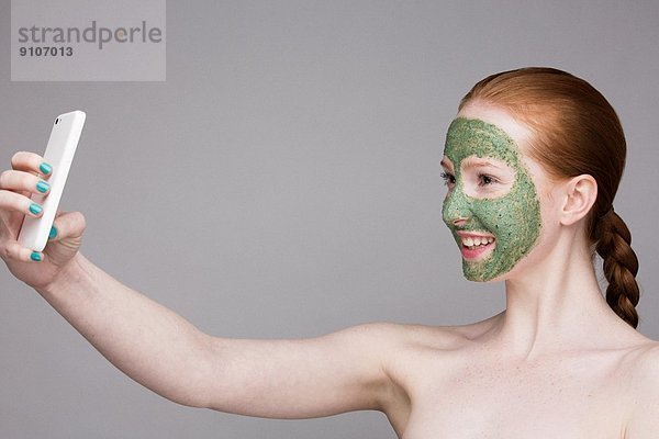 Junge Frau mit Gesichtsmaske  Selbstporträtfotografie mit Smartphone