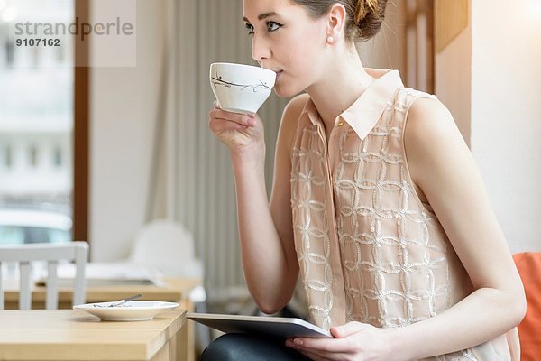 Junge Geschäftsfrau im Café  die Kaffee trinkt und digitale Tabletten benutzt
