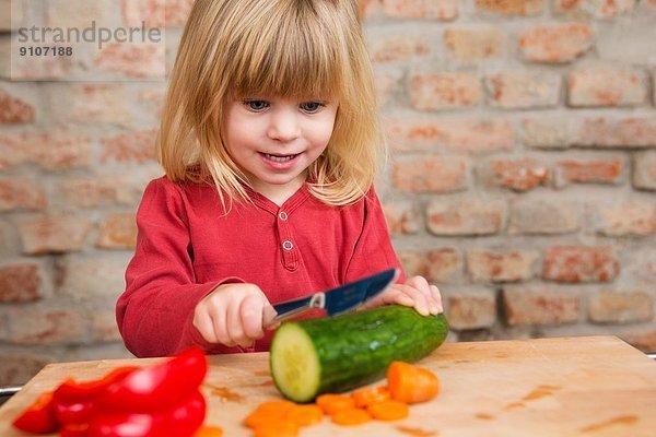 Zweijähriges Mädchen in der Küche lernt Gemüse zu schneiden