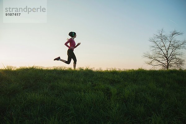 Junge Läuferin mit Silhouette auf dem Hügel