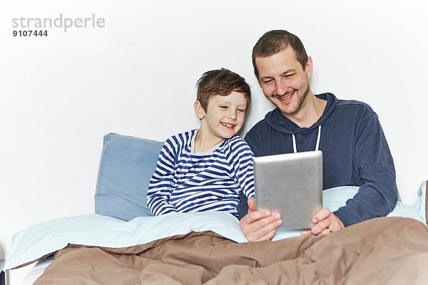 Vater und Sohn mit digitalem Tablett im Bett