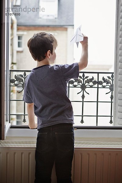Junge startet Papierflugzeug aus dem Fenster