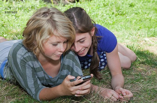 Teenager-Mädchen auf Rasen liegend  mit Smartphone