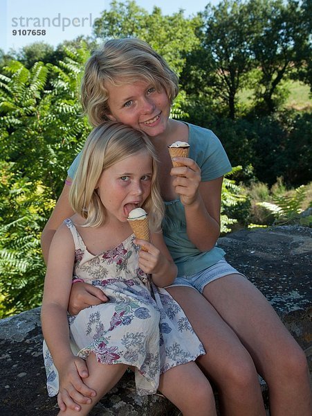 Schwestern sitzen im Garten und essen Eis.