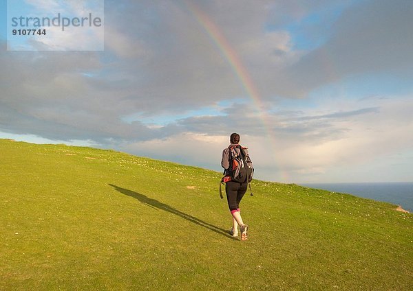Junge Wanderin wandert bergauf Richtung Regenbogen
