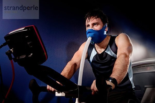 Mittlerer erwachsener Mann in Gesichtsmaske im Fitnessstudio im Höhenzentrum