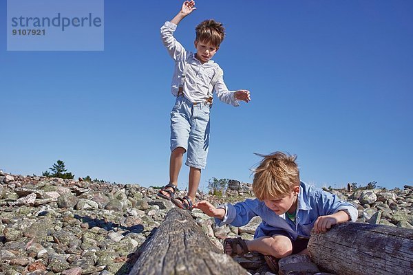 Zwei Jungen spielen auf Treibholz am Strand