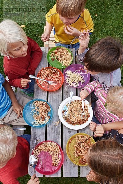 Blick über den Kopf von sieben Kindern  die Spaghetti am Picknicktisch essen