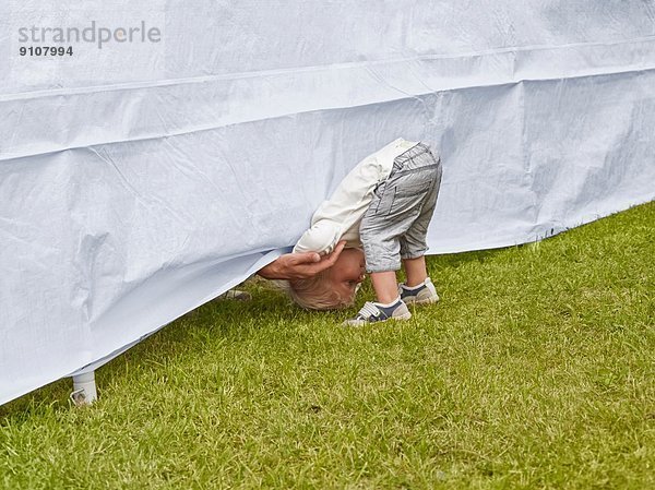Junge  der sich nach vorne beugt  um die Hand des Vaters unter dem Zelt zu erreichen.