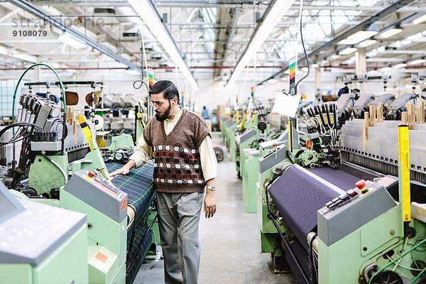 Männlicher Fabrikarbeiter überwacht die Qualität der Webmaschine in der Wollmanufaktur