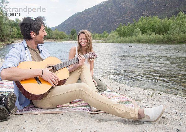 Freunde sitzen am Fluss und spielen Gitarre