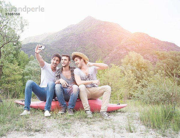 Drei junge Männer sitzen auf dem Kanu und fotografieren sich selbst.