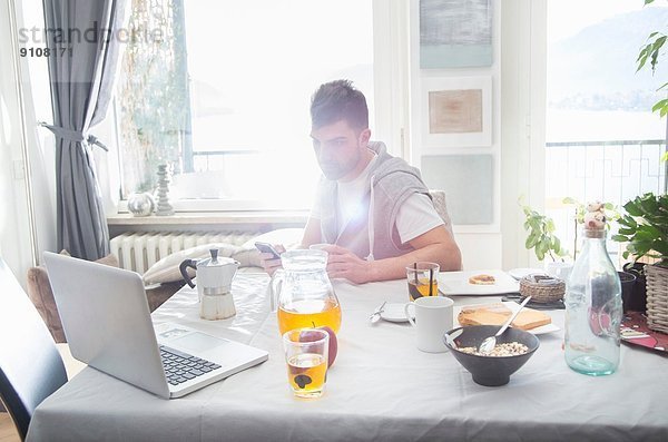 Junger Mann beim Frühstück und mit Laptop