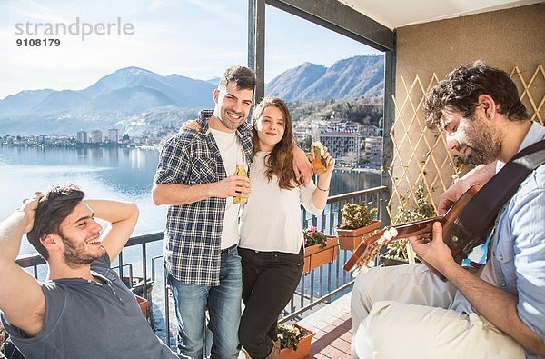 Vier Freunde auf dem Balkon  mit Gitarre und Bier